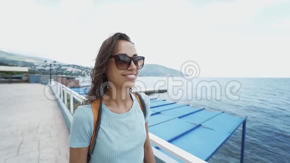 穿着黑色泳衣和白色帽子的漂亮性感运动女人在海边沿着海湾散步的外部肖像视频的预览图