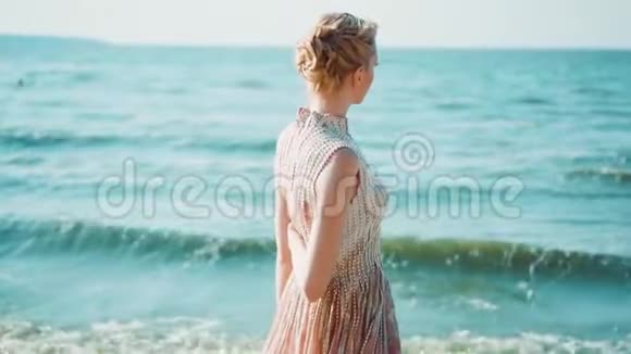 美丽的女孩穿着浅粉色的长裙独自一人留在岛上靠近蓝色的大海把她的手放在身后视频的预览图