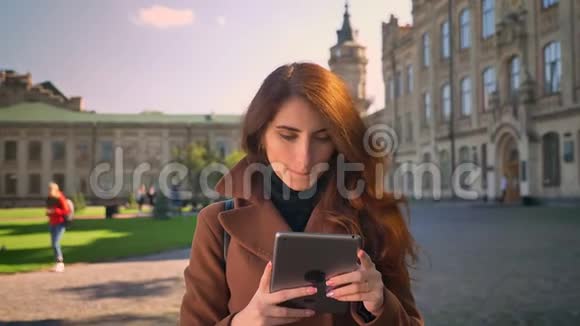 可爱快乐的加拉加斯黑发女人看着平板电脑边站在户外边聊天边挥舞着网络摄像机视频的预览图