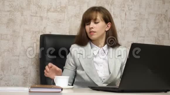 漂亮的女孩坐在办公室的椅子上喝咖啡茶在笔记本电脑上聊天年轻女子视频的预览图