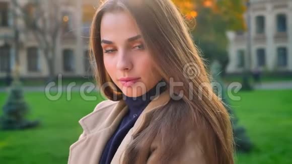 可爱的白种人女性平静地站着在户外的阳光下在城市背景下看着摄像机的寒冷和害羞视频的预览图