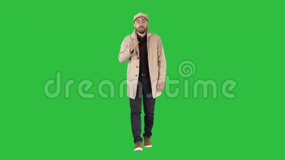 英俊的男人穿着浅色战壕外套与相机焦点交谈并思考它在绿色屏幕上的手势Chroma键视频的预览图