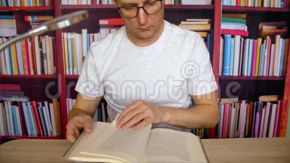 一个戴眼镜的人在家图书馆里坐在台灯旁看书视频的预览图