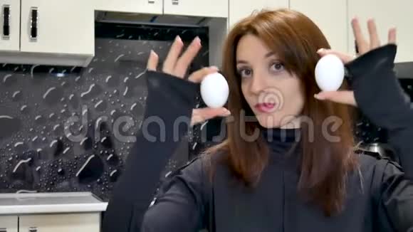 穿着黑色衬衫的年轻女子展示着两个鸡蛋坐在厨房里视频的预览图