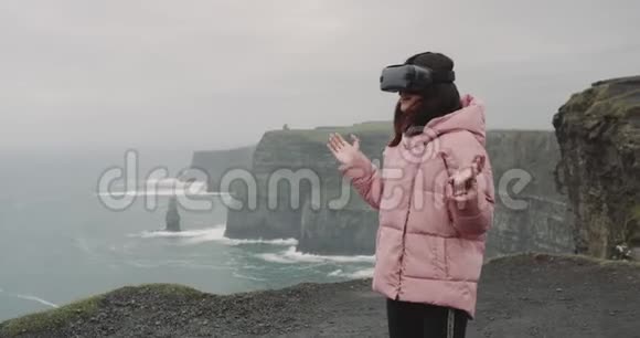 一位年轻的女士在悬崖顶上戴着虚拟现实眼镜她非常印象深刻用手触摸视频的预览图