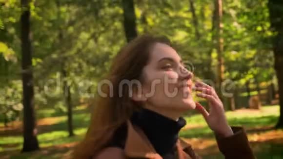 可爱的黑发白种人白种人女人在公园里看着阳光在背景上看着绿树微笑着视频的预览图