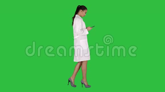 开朗可爱的年轻女性医生在绿色屏幕上行走时在手机上键入文字Chroma键视频的预览图