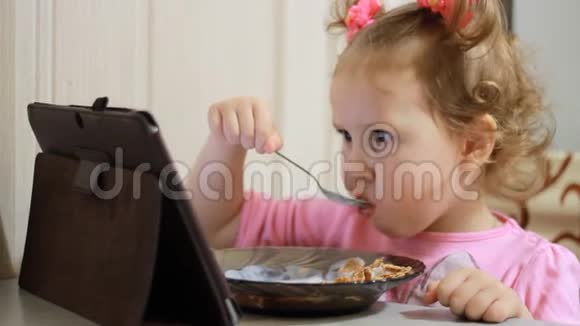 小女孩吃早餐涂酸奶并在平板电脑屏幕上锁定视频视频的预览图