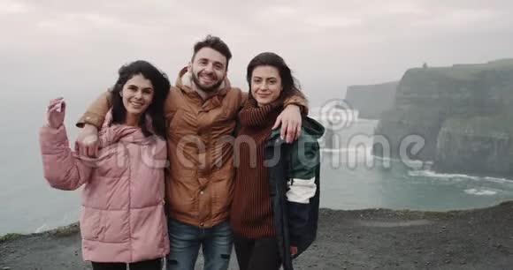 快乐的三位游客朋友在镜头前摆姿势在令人惊叹的悬崖峭壁上拍照留念视频的预览图