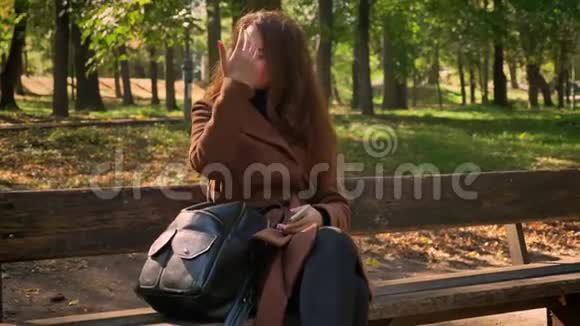 在阳光明媚的户外公园里坐在一个白种人深色头发的长凳上享受着纯净的自然视频的预览图