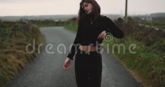 在乡间小路上一位瘦小的年轻女士在镜头前热烈地跳舞她闭上了眼睛移动着视频的预览图