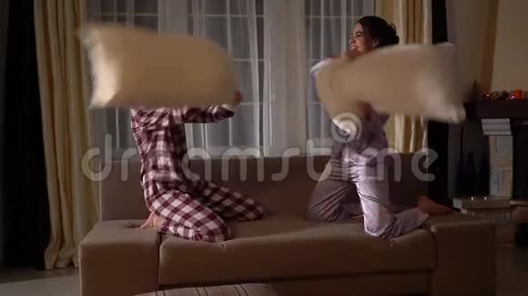 晚上两个双胞胎姐妹在舒适的客厅里笑着玩抱着枕头打架视频的预览图