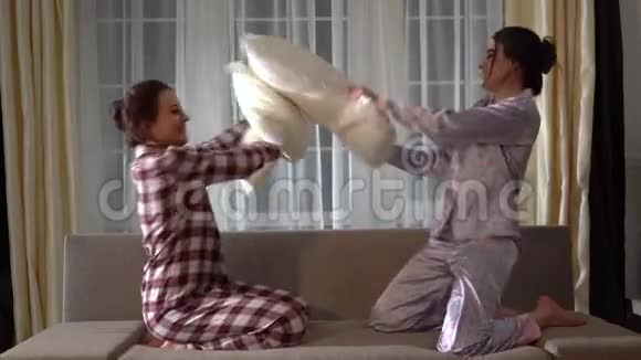 两个双胞胎姐妹在舒适的客厅里欢笑着玩晚上用枕头打架视频的预览图