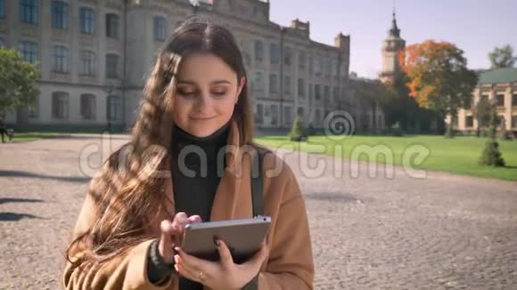 快乐的白种女人站在城市里带着快乐的微笑和冷静随意的神情展示着蓝色的屏幕视频的预览图