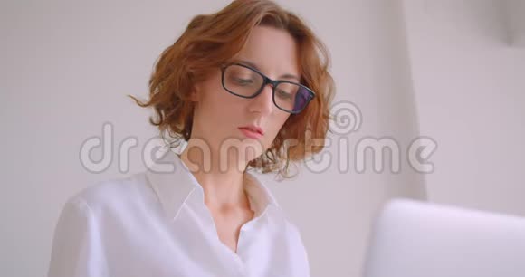 戴着眼镜的红发白种人女商人的特写镜头她用笔记本电脑看着镜头开心地笑着视频的预览图