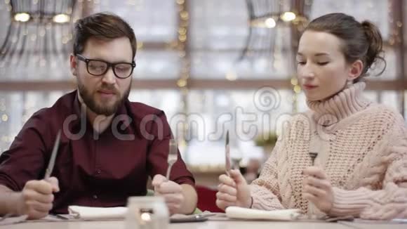 男人和女人静静地坐在桌子旁等待着拿着刀叉的饭菜视频的预览图
