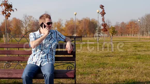 年轻时尚和时髦的人戴着黑色眼镜坐在长凳上在电话上说话特写复制空间慢动作视频的预览图