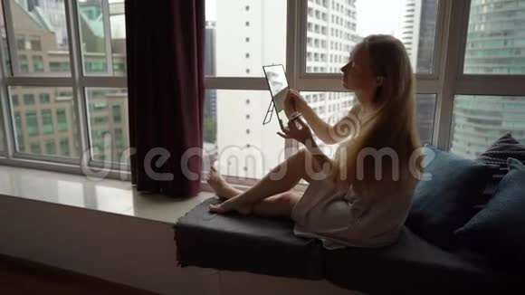 一位年轻女子坐在市区的一扇全景窗旁化妆的超慢动作镜头视频的预览图