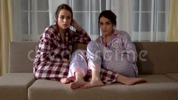 两个双胞胎穿着睡衣坐在沙发上看恐怖电影关系姐妹视频的预览图