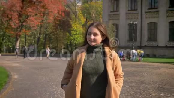 美丽的白种人女人走在阳光明媚的城市里带着可爱的微笑秋天的气息绿色的背景运动摇摆着视频的预览图