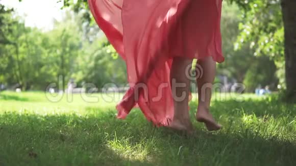穿着红色连衣裙的女孩赤脚在草地上旋转女性腿部特写视频的预览图