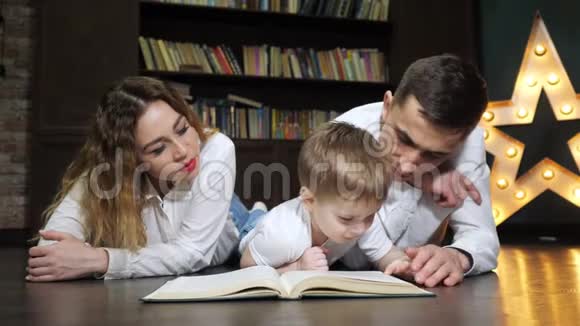 年轻的家庭母亲儿子和爸爸的肖像正在一起读一本书视频的预览图