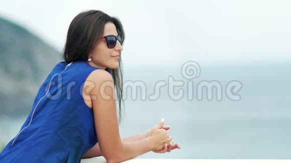 在阳台或露台上观看迷人的时尚女性太阳镜欣赏海景视频的预览图