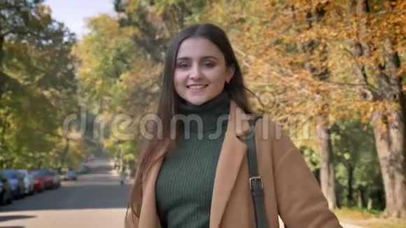 微笑着令人敬畏的白种人女性正享受着阳光明媚的秋日快乐地看着相机站在和视频的预览图