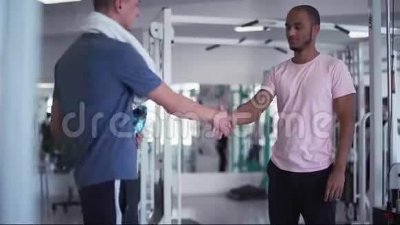 美国黑人和白人在健身房握手两个年轻人在健身房健身视频的预览图