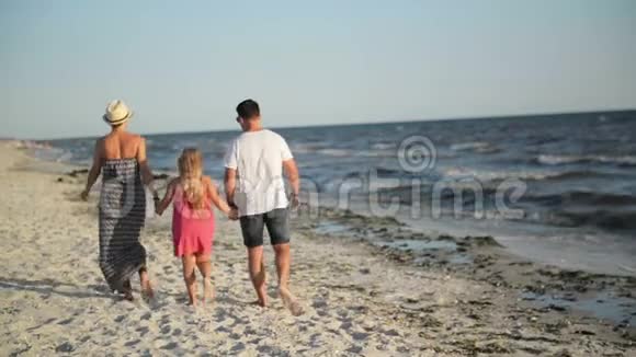 带着小女儿在海滩散步在海滨避暑时牵手的幸福家庭的后景视频的预览图