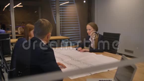 在现代化的办公室里三名工作人员在桌子旁看着图纸和谈话视频的预览图