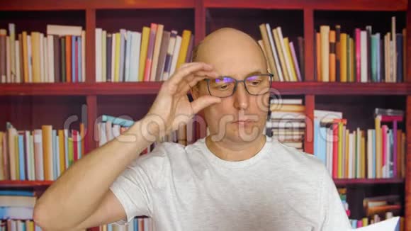 思考人戴眼镜看书在家书库的书柜背景在舒适的家中阅读文档的男人视频的预览图