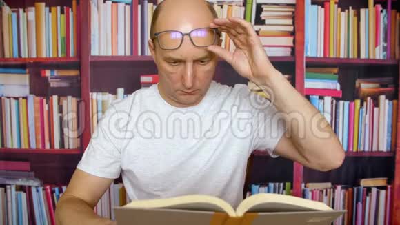 一个戴眼镜的人在书架背景下的家庭办公室桌上看书视频的预览图