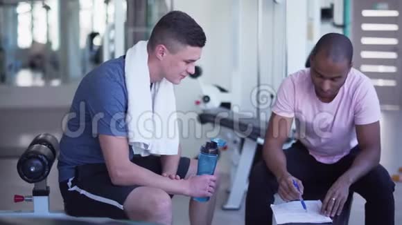 一个美国黑人和一个白人交谈教练给健身中心的人提供健身疗法视频的预览图