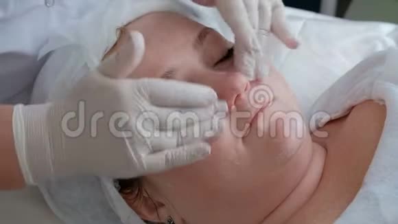 美容中心的美容师在手术过程中用白手套的手一个胖女孩的面部按摩视频的预览图