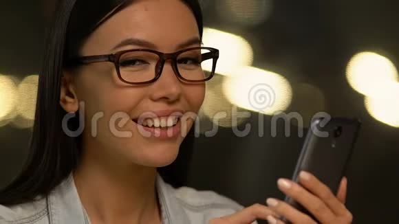 微笑的年轻女士拿着智能手机看着相机现代科技视频的预览图