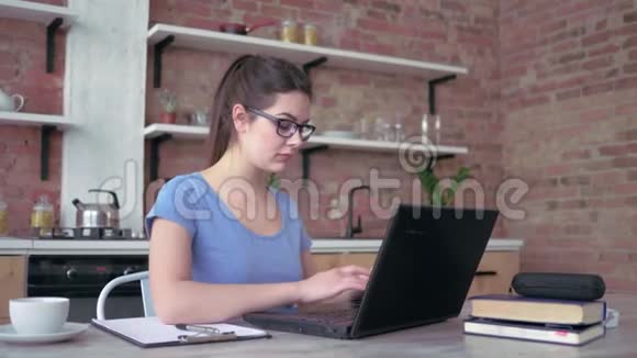 自由职业者女孩戴眼镜在笔记本电脑键盘上打字在网上工作时在剪贴板上写笔记视频的预览图