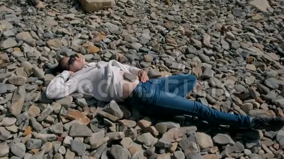 戴墨镜的女人在秋天躺在石滩上石头在女孩肚子上视频的预览图