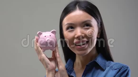 年轻的亚洲女人摇着储蓄罐省钱投资关门视频的预览图