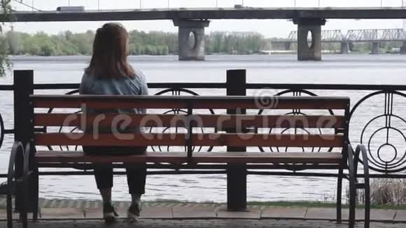 孤独的女孩坐在公园的长凳上看着工业景观视频的预览图