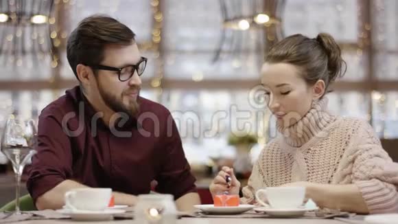 年轻女子正和丈夫坐在一起时在一家餐馆里给丈夫点了一块小蛋糕视频的预览图