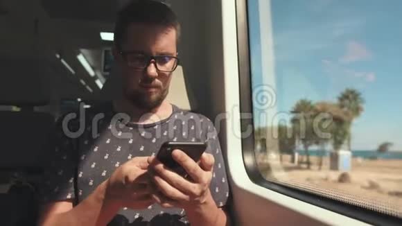 男乘客正在通过手机发送短信并在列车窗口看着视频的预览图