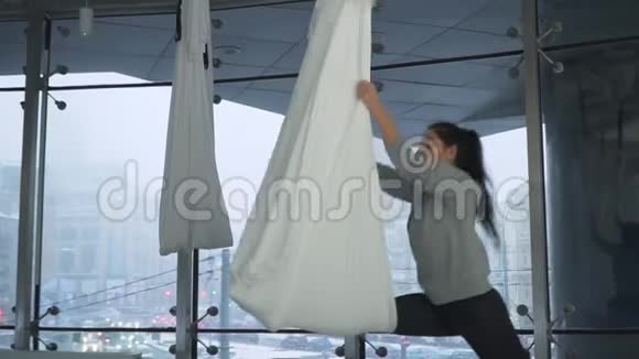 美丽的女人在空中转过来手里拿着瑜伽吊床周围有许多白色的空吊床现代视频的预览图