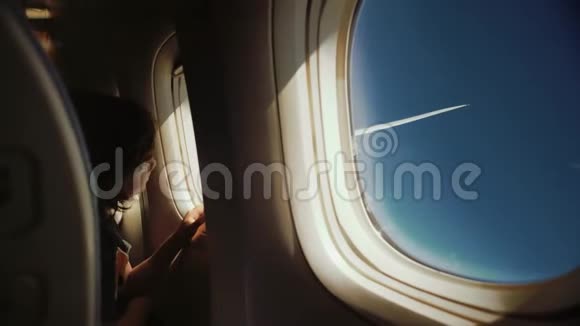 可爱有趣的小孩在飞行时看着窗户坐在靠近窗户的座位上阳光透过窗户照射进来视频的预览图