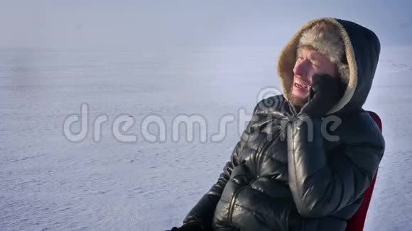 穿着保暖外套头罩的商人在雪地里的特写肖像在手机上愉快地交谈视频的预览图