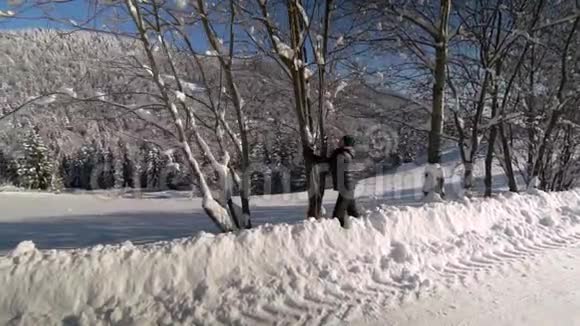 一个年轻人穿过雪山森林他从树上摇雪他很快乐笑得很有趣慢动作视频的预览图