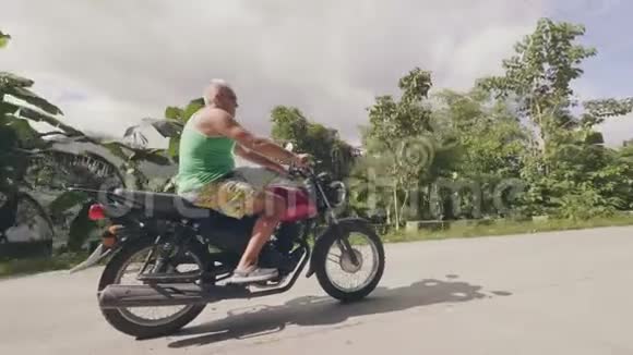 成熟男子骑摩托车骑摩托车在乡村道路上的热带棕榈树景观高级官员旅行视频的预览图