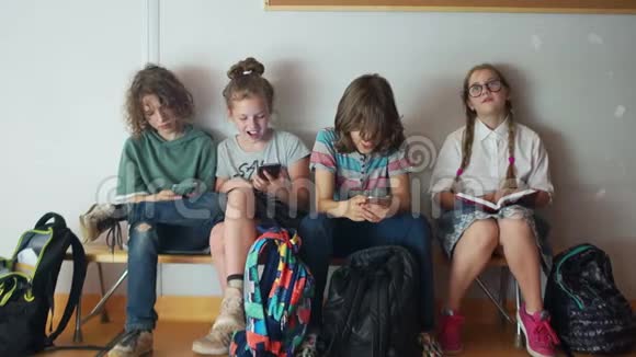 三个青少年对他们的手机充满热情最好的学生坐在他们旁边读一本书小学生和小学生视频的预览图