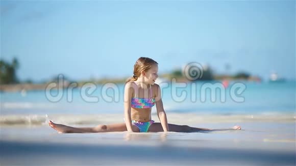 可爱活泼的小女孩正坐在雪白沙滩上的一根树枝上视频的预览图