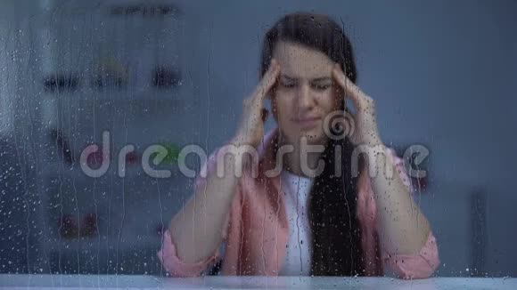 精疲力竭的中年女士在雨窗后按摩太阳穴偏头痛视频的预览图